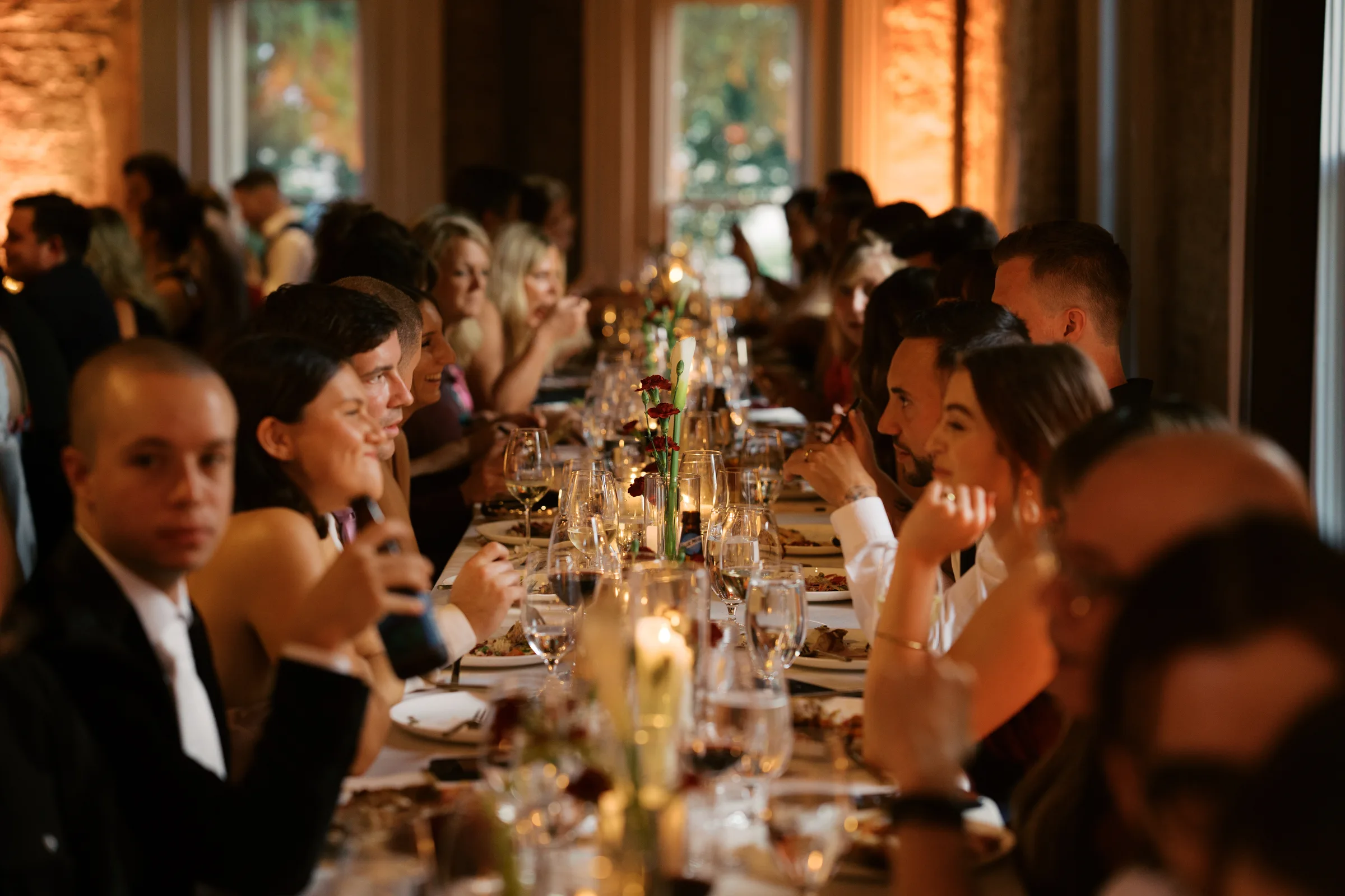 Wedding guests laughing along a candlelit banquet table