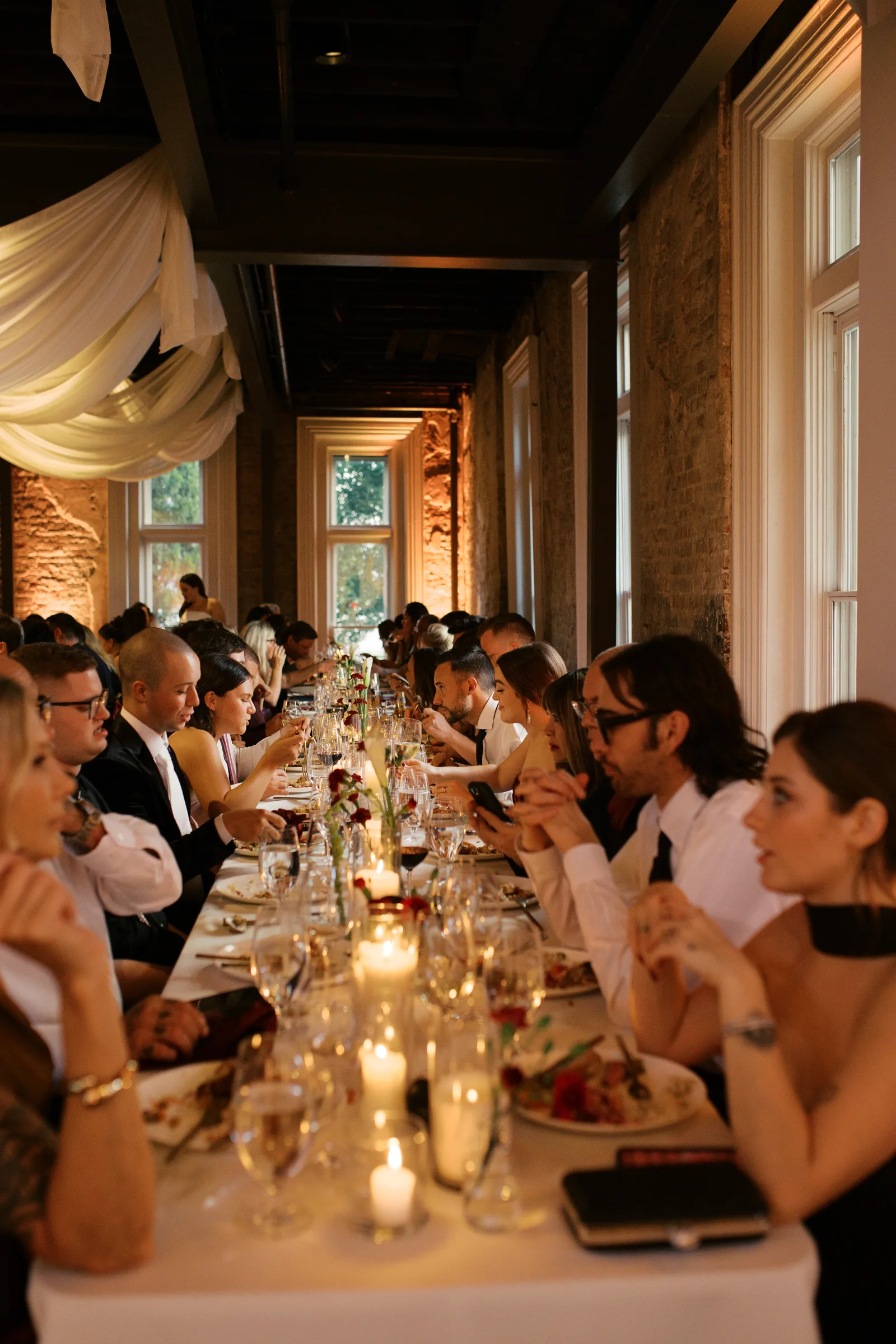 Reception hall full of guests at a long table under draped fabric