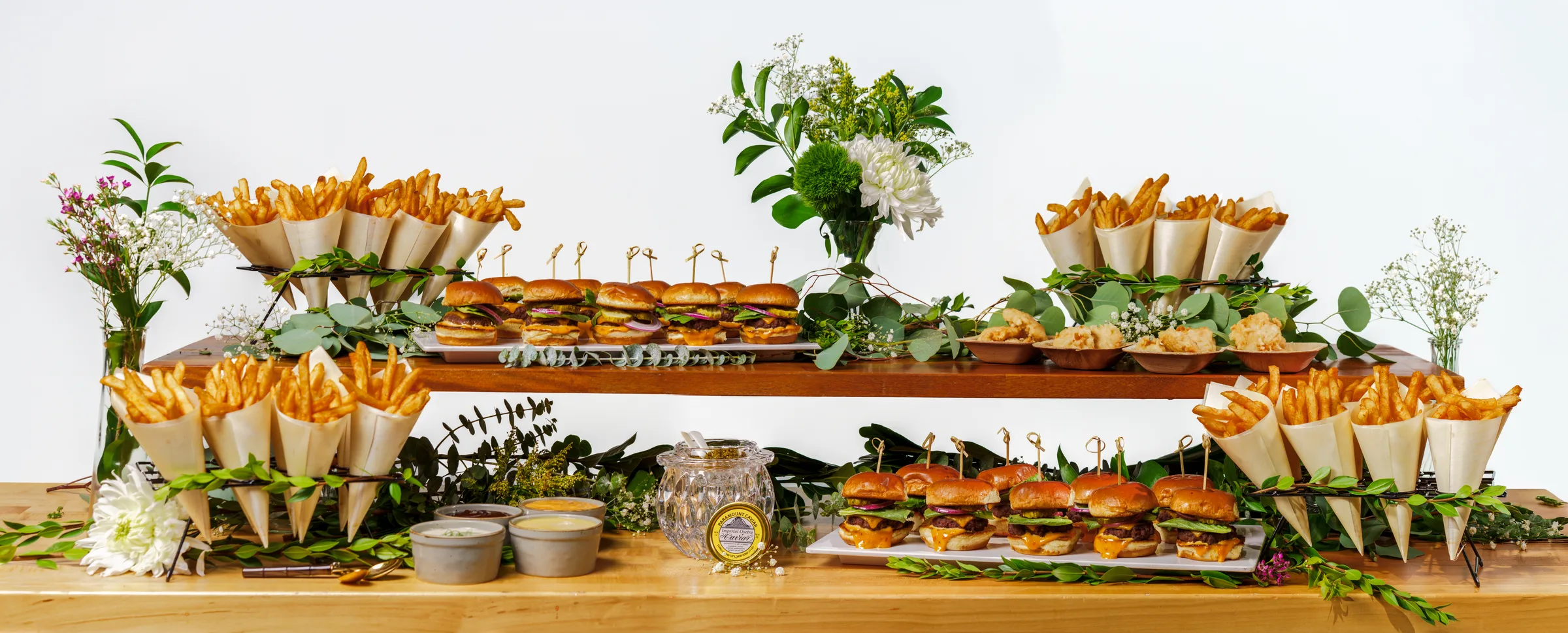 Tiered station of sliders, fries cones, and dipping sauces on a butcher-block table