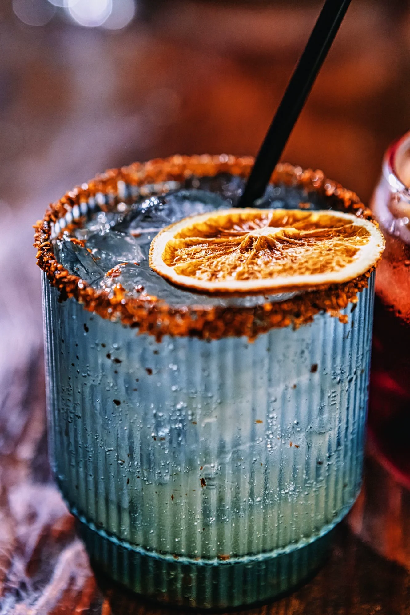 Spiced-rim cocktail in a ribbed glass with ice and a dehydrated orange wheel